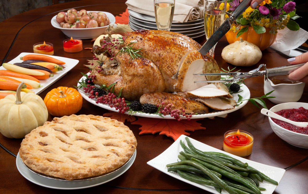 A Thanksgiving table: the turkey being carved, apple pie, green beans, cranberry sauce and two glasses of sparkling wine
